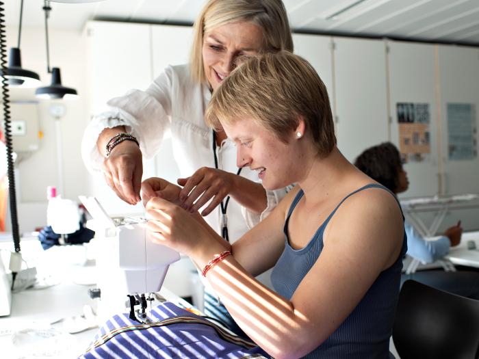 Underviser hjælper en ung med at sy på symaskine i Design.